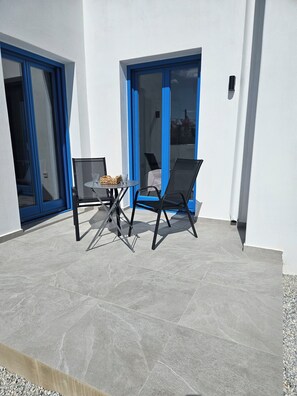 A patio with a table and two chairs, a glass door, and a blue frame. - One-bedroom apartment "Achinos" in Agkairia with AC and traditional comfort (Aliki)