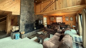 Een gezellig blokhutinterieur met een stenen openhaard, houten plafond en een ruime bank.