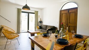 Un coin repas avec une table en bois dressée pour deux personnes, une chaise jaune et un canapé en arrière-plan.