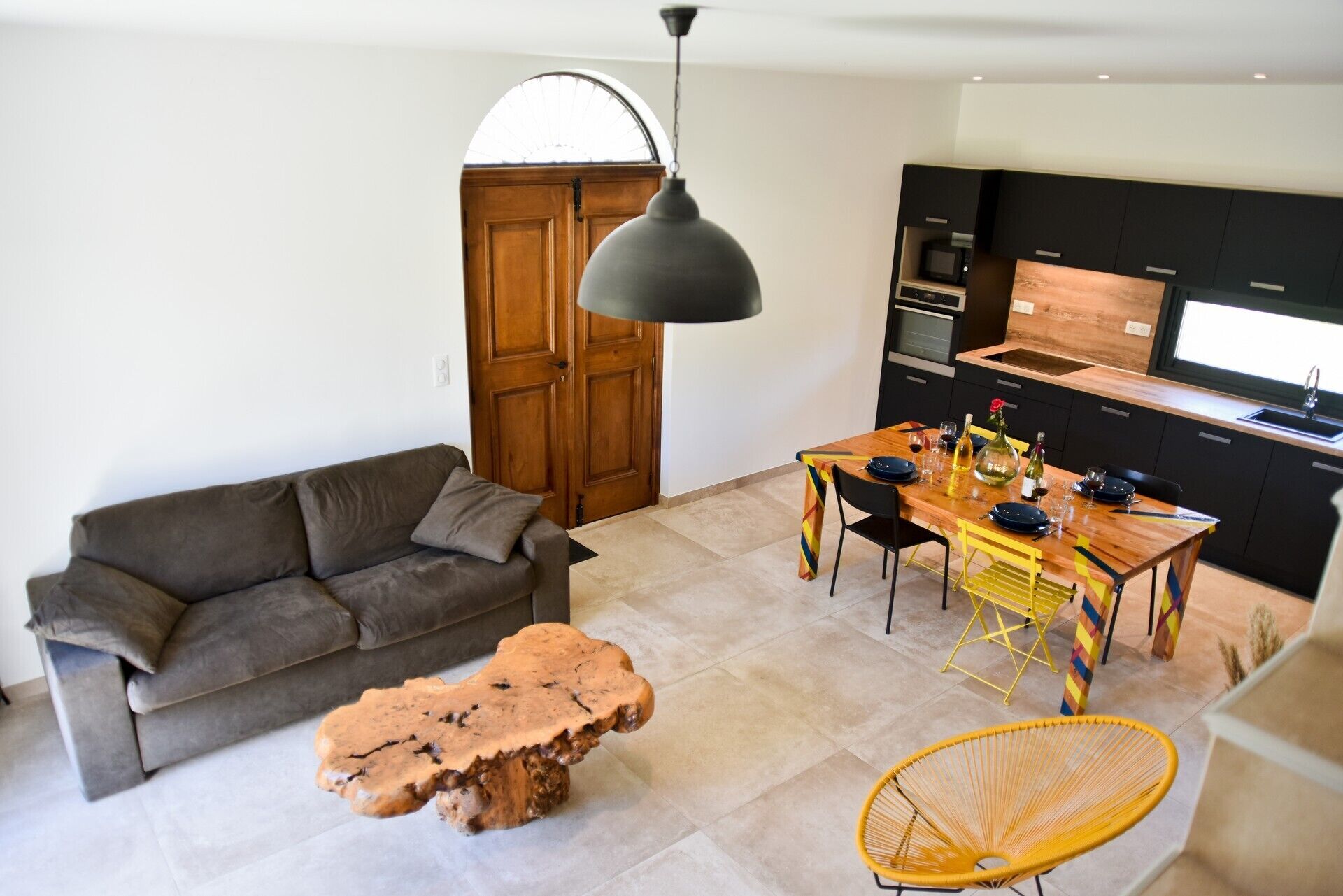 Una sala de estar moderna con un sofá, una mesa de centro de madera, una mesa de comedor con sillas y una zona de cocina con microondas y fregadero.