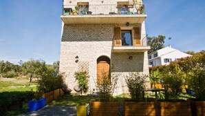Un bâtiment en pierre de deux étages, doté d’un balcon, d’une porte en bois et d’un petit jardin agrémenté de plantes et de quelques sièges.