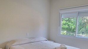 Ein Schlafzimmer mit einem Bett, einem Nachttisch, einem Fenster und einer Deckenleuchte.