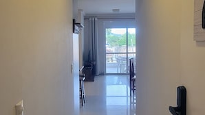 Ein Korridor mit einer Tür rechts, der zu einem Balkon mit Blick auf Grün führt.