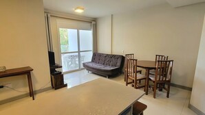 Ein gemütlicher Wohnbereich mit einer Couch, einem Esstisch und Stühlen. Ein großes Fenster lässt viel Tageslicht herein und bietet einen Ausblick ins Freie.