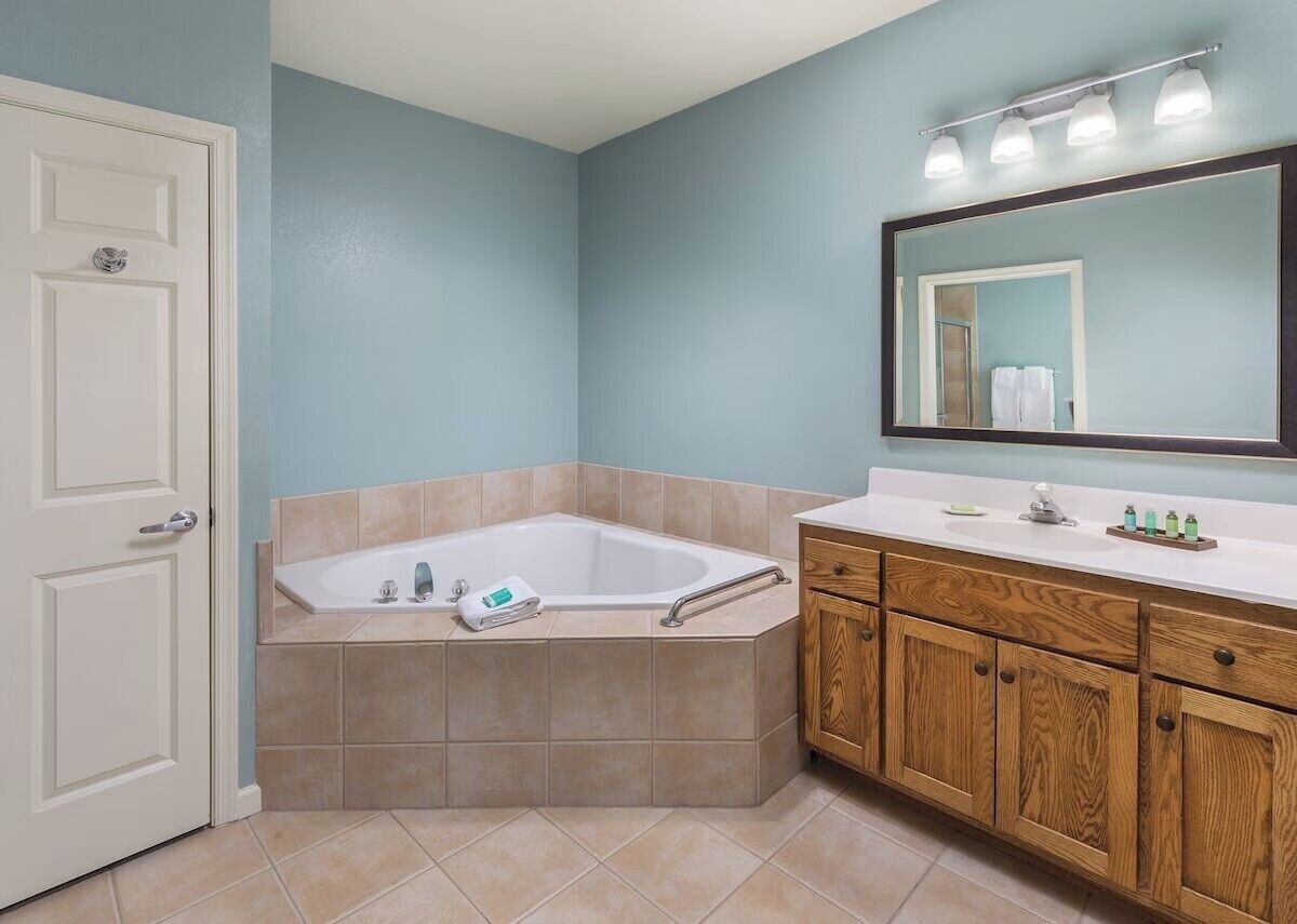 Un bagno con vasca, mobili in legno, una porta bianca e uno specchio illuminato.