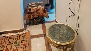 Una stanza con pavimento a scacchi, un tavolo rotondo con piano in marmo, un televisore montato a parete e un piccolo mobile con specchio.