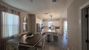 Une cuisine moderne avec des meubles blancs, un îlot central et un coin repas comprenant une table en bois et des chaises blanches.