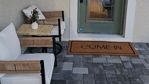 Une entrée moderne avec une porte verte, un paillasson et un petit espace extérieur aménagé avec des meubles en osier.