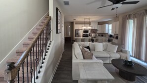 Un vaste espace de vie comprenant un escalier, un ensemble de canapés blancs, une table basse et un ventilateur de plafond.