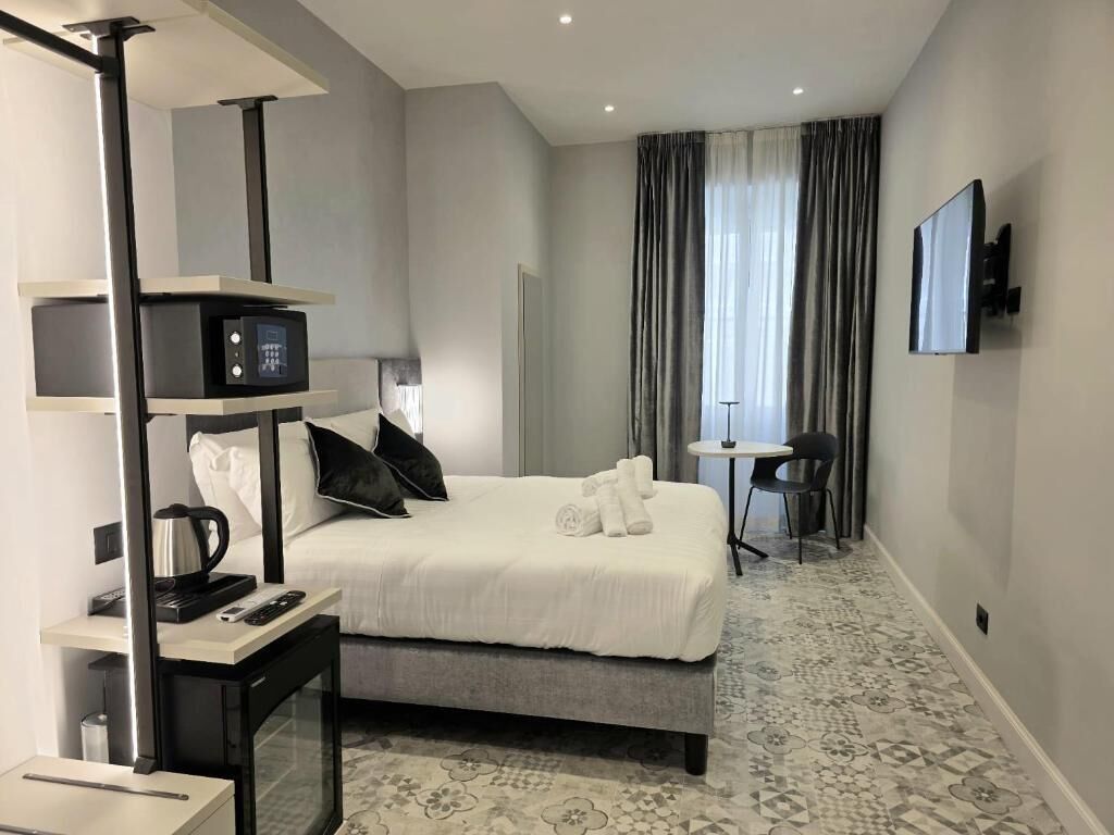Una habitación de hotel moderna con cama, mesita de noche, lámpara y televisor de pantalla plana.