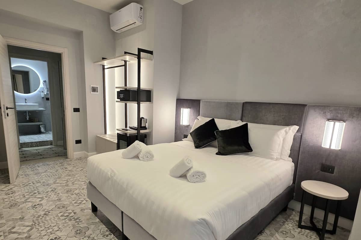 A modern hotel room with a large bed, a bedside table, a small round table, and a walk-in closet.