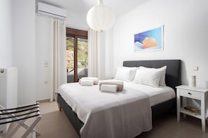 Ein modernes Schlafzimmer mit einem großen Bett, einem Nachttisch, einem Sessel und Blick ins Freie.