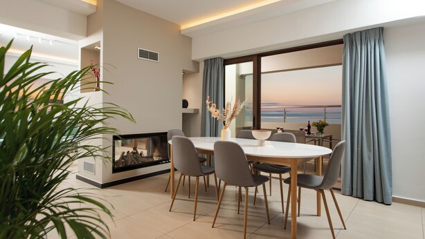 A modern dining area with a round table, grey chairs, and a fireplace.