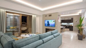 A modern living room with a grey sofa, a flat-screen TV, and a dining area with a kitchen in the background.