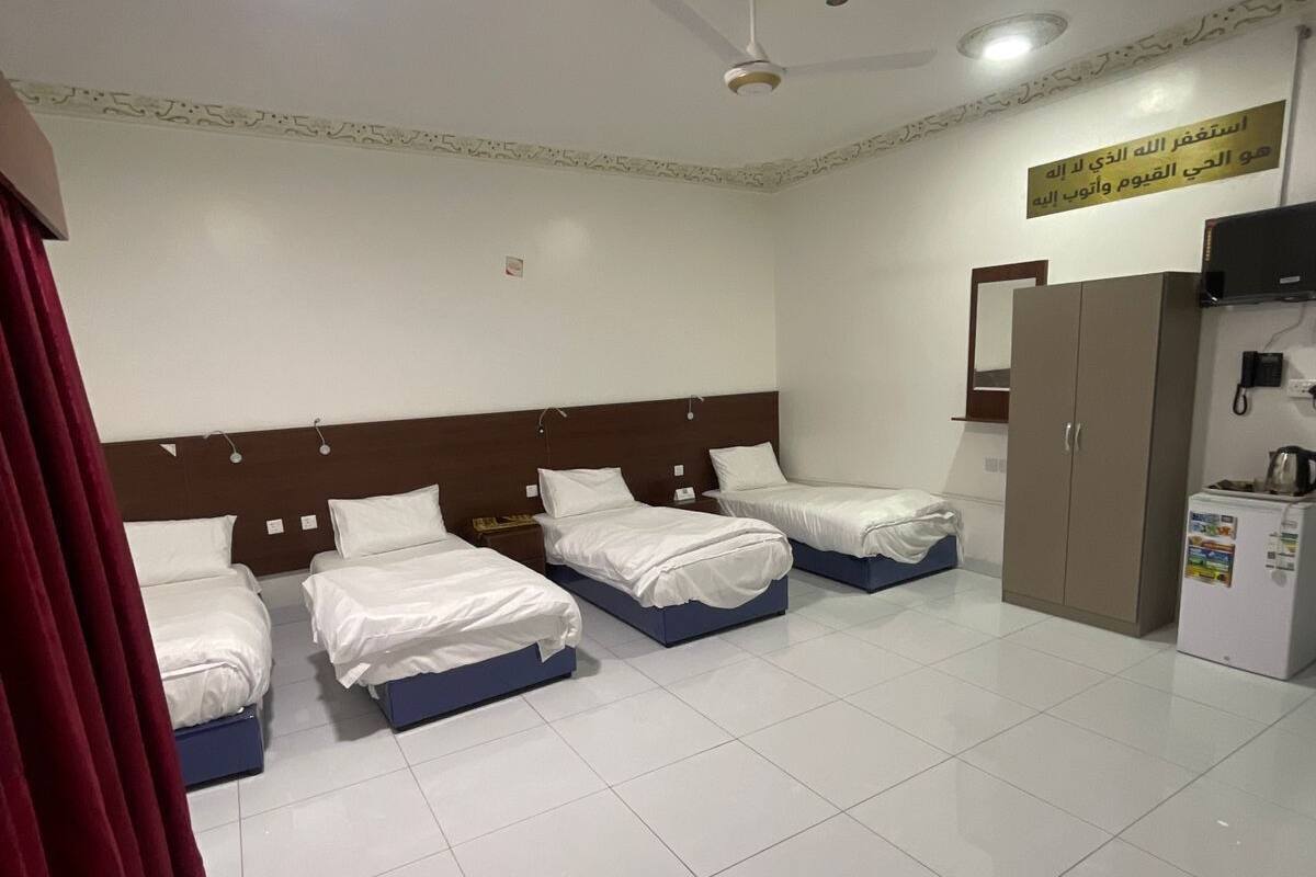 Ein Hotelzimmer mit drei Einzelbetten, einem Deckenventilator, einem Fernseher und einem Kühlschrank.