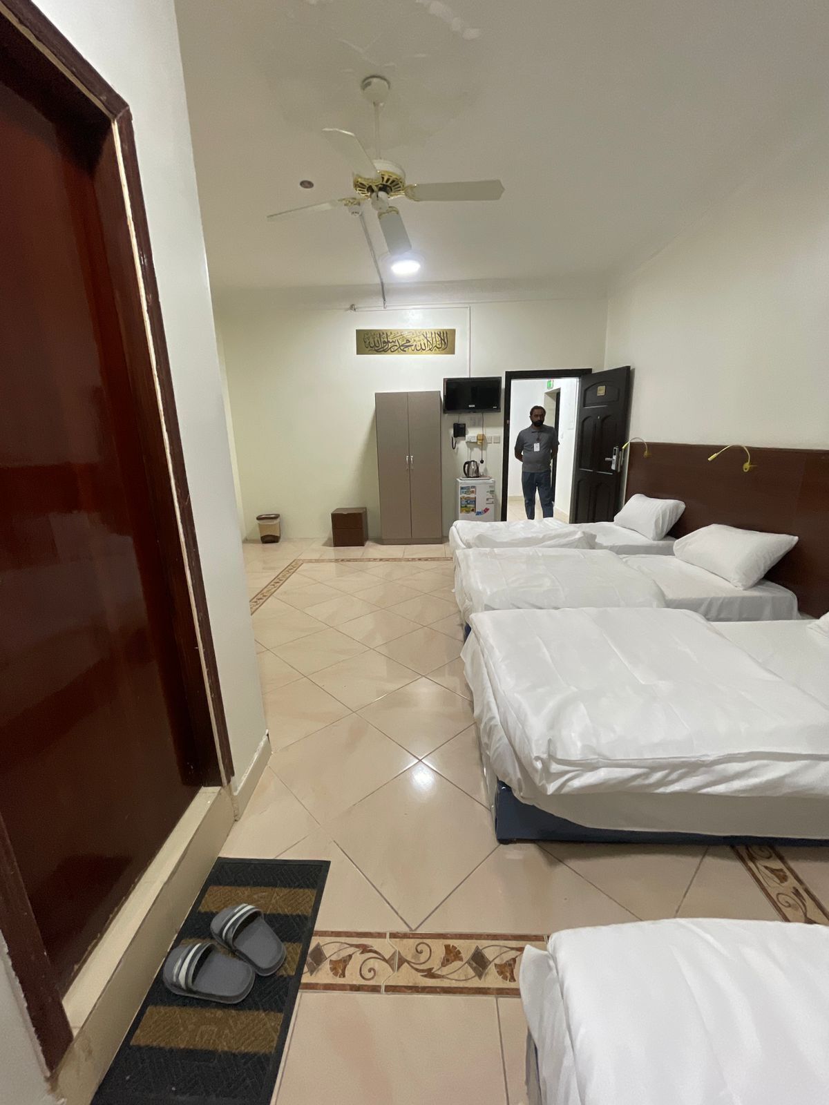 Une chambre d’hôtel avec deux lits, un ventilateur de plafond, une télévision, une armoire et une petite kitchenette.