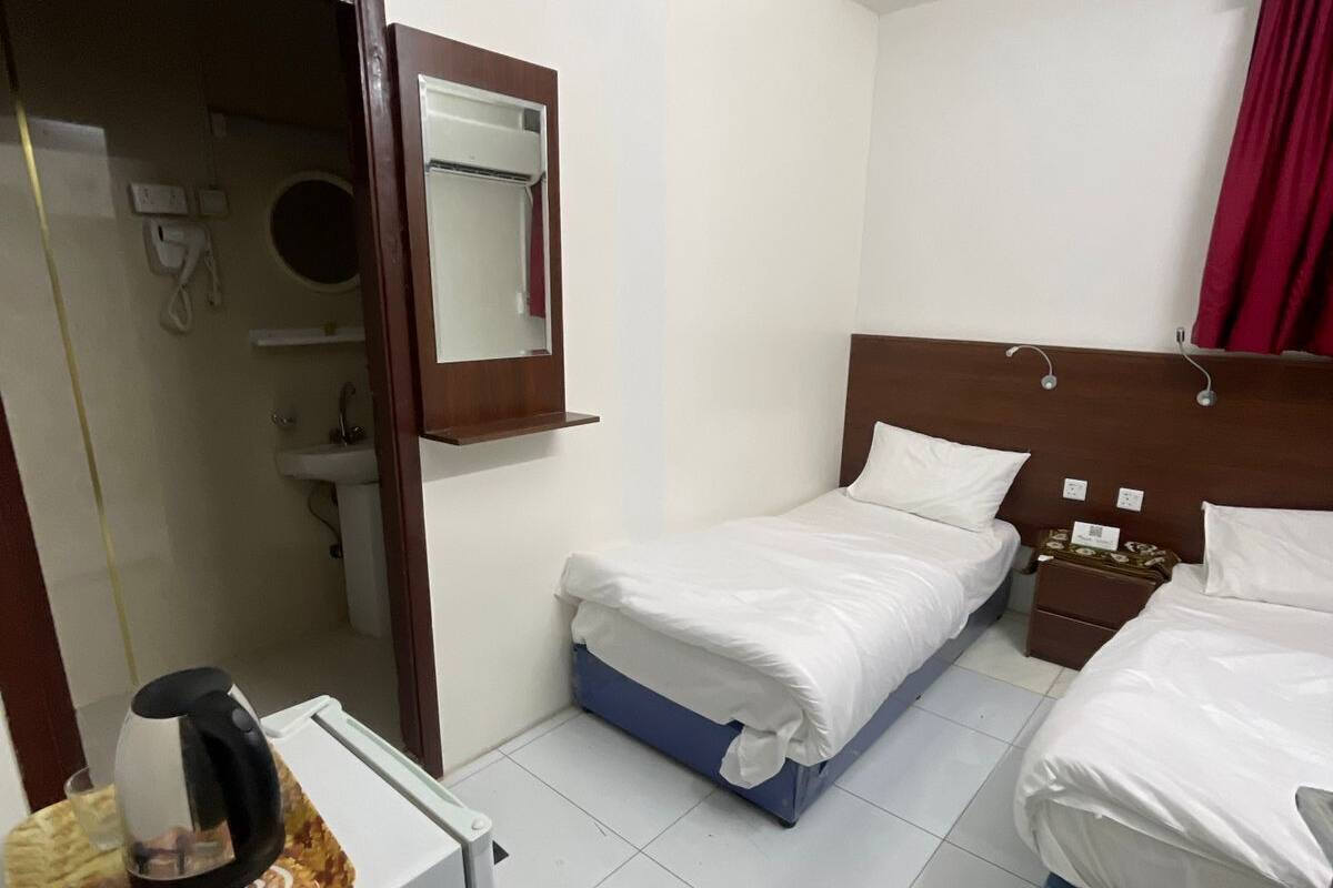 Ein Hotelzimmer mit zwei Einzelbetten, einer kleinen Küchenzeile, einem Spiegel und einem Deckenventilator.