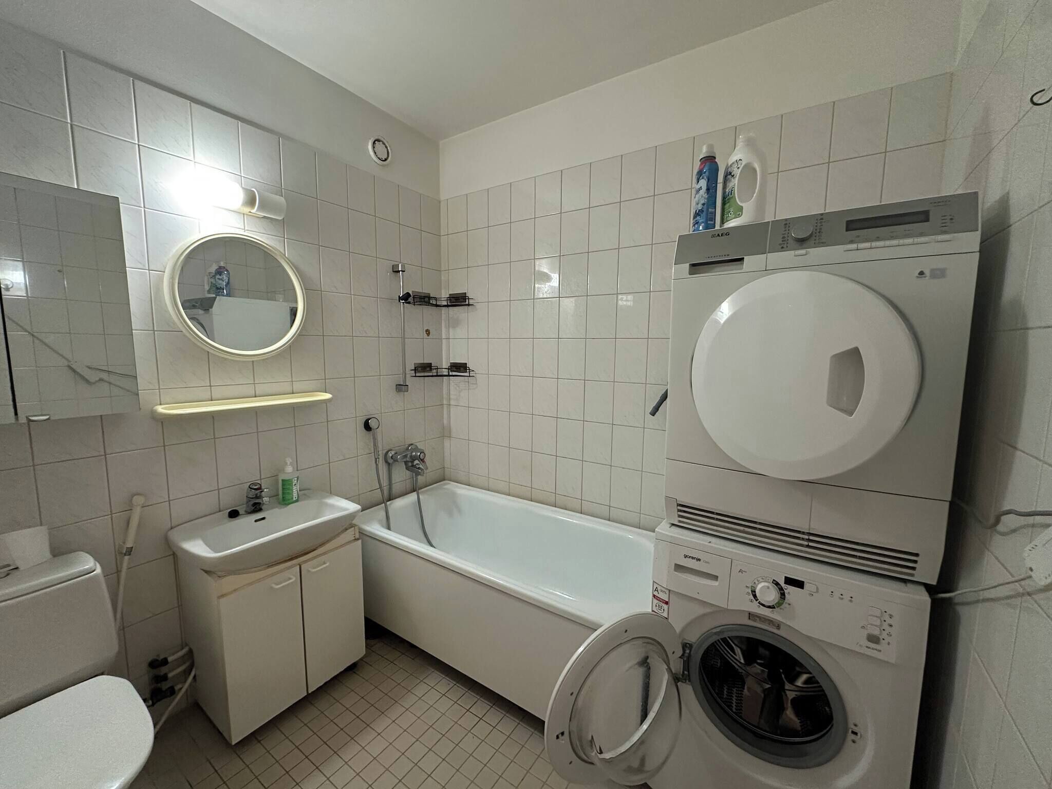 A bathroom with a toilet, sink, mirror, shower, and a stacked washer and dryer.