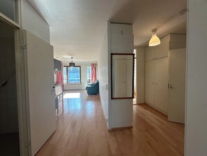 Un hall d’entrée spacieux avec un plancher en bois, un fauteuil bleu, un grand miroir et une armoire.