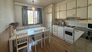 A modern kitchen with white cabinets, a dining table with chairs, a stove, and a window with curtains. - Spacious 2 Bedroom 75 sqm Kannelmäki (Helsinki)