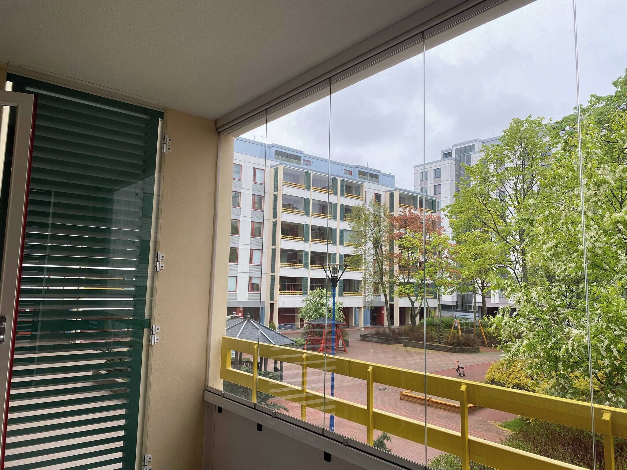 A balcony with a view of a courtyard, featuring modern buildings and a tree.