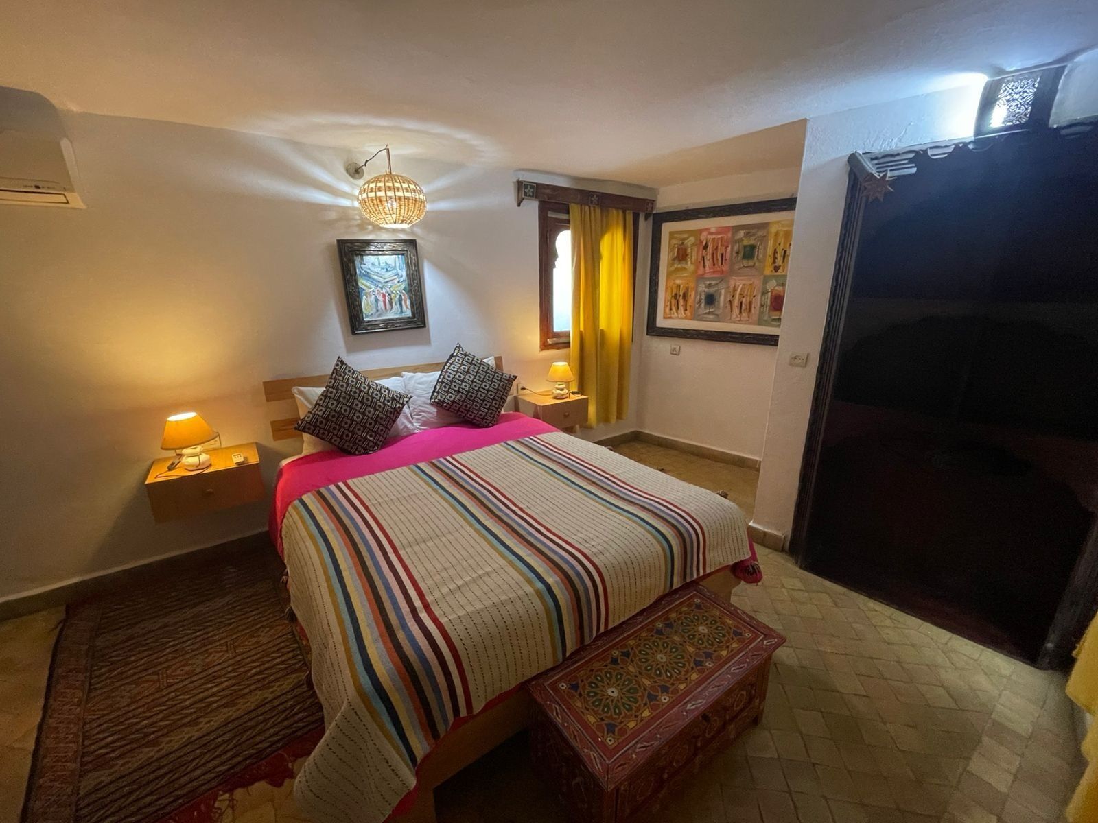 Ett hotellrum med en säng, sänglampor, en dekorativ matta, ett litet bord och ett konstverk som hänger på väggen.