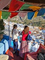Un balcón con banderas coloridas, vista a un pueblo de edificios blancos y una persona con un vestido rojo.