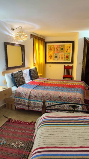 A bedroom with two beds, a large mirror, a framed artwork, and a chair. - Dar Sababa (Chefchaouen)