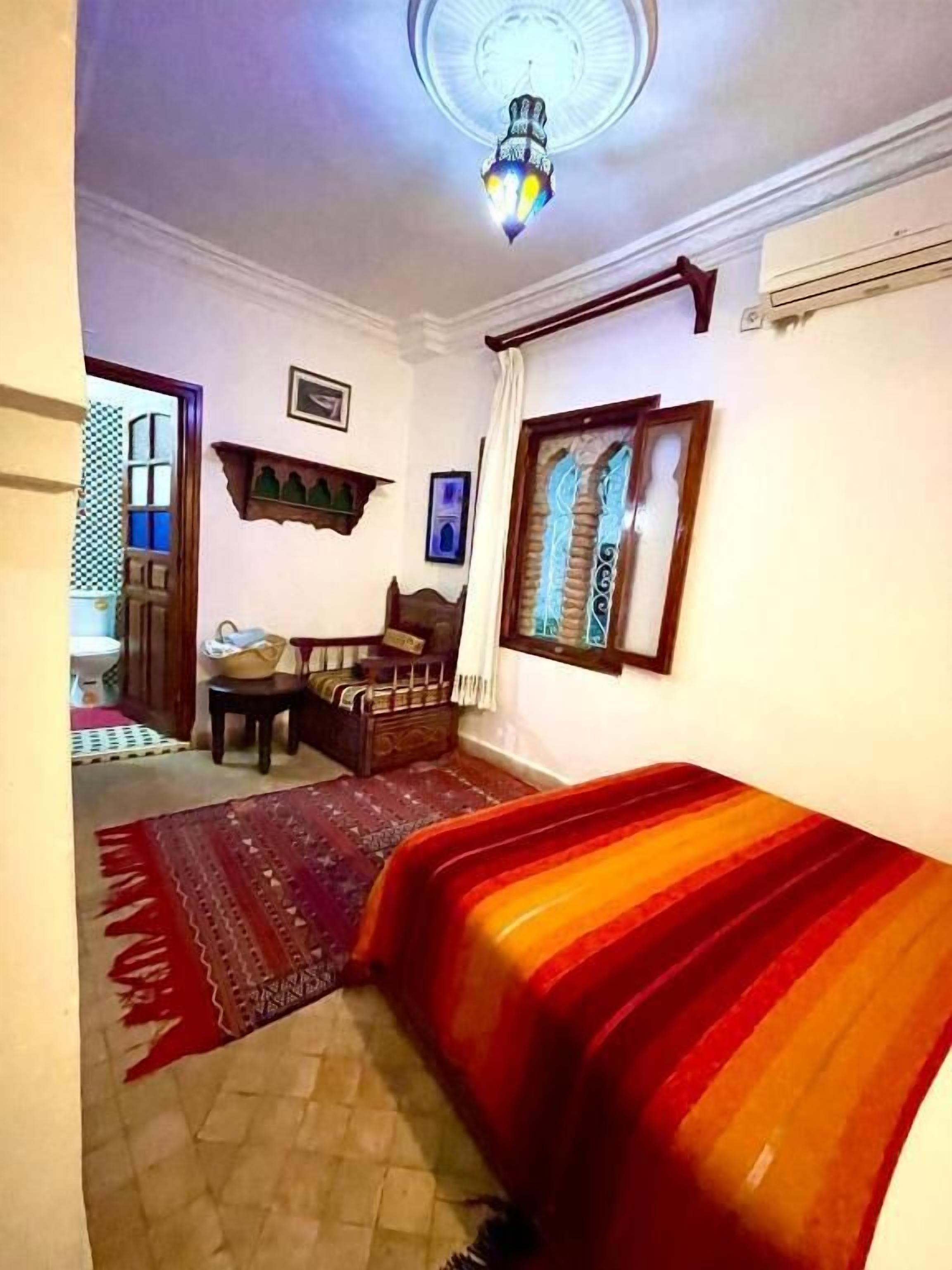 Une pièce comprenant un lit, une chaise en bois, une petite table, un tapis et un luminaire au plafond.