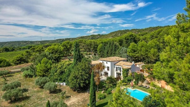 Una vila amb piscina, envoltada de vegetació exuberant i turons.