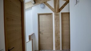 Un passadís amb portes de fusta, una escala i un sostre amb bigues al descobert.