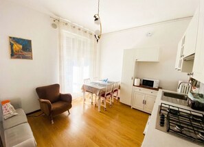 Een knus woongedeelte met een eethoek, kitchenette en een enkele bruine fauteuil.