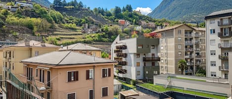 A residential area with multi-story buildings, a visible church on a hill, and a mountainous backdrop.