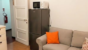 A compact living space with a grey sofa, a small white cabinet, and a grey refrigerator. - "Valeri" Vacation Rental in Sondrio - Peaceful Stay Near City Center (Sondrio)