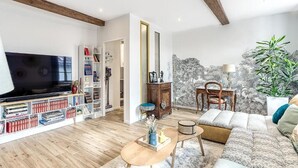 A modern living room with a large flat-screen TV, a bookshelf, a sofa, and a dining area. - La demeure de Gab  (Trévoux)