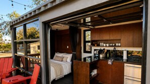Una camera moderna e compatta con un letto, angolo cottura e una piccola area salotto con sedie rosse.