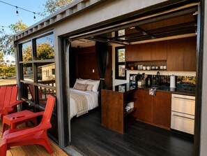Ein kompakter, moderner Raum mit Bett, Küchenzeile und einer kleinen Sitzecke mit roten Stühlen.