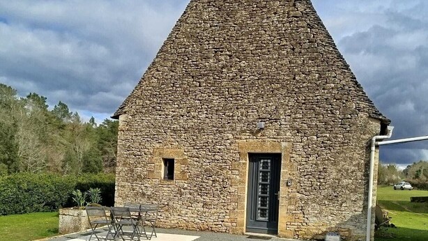 A stone building with a conical roof, a door, and a small porch area with a table and chairs. - Accommodation in a small character house in SAINT GENIES (Saint-Geniès)
