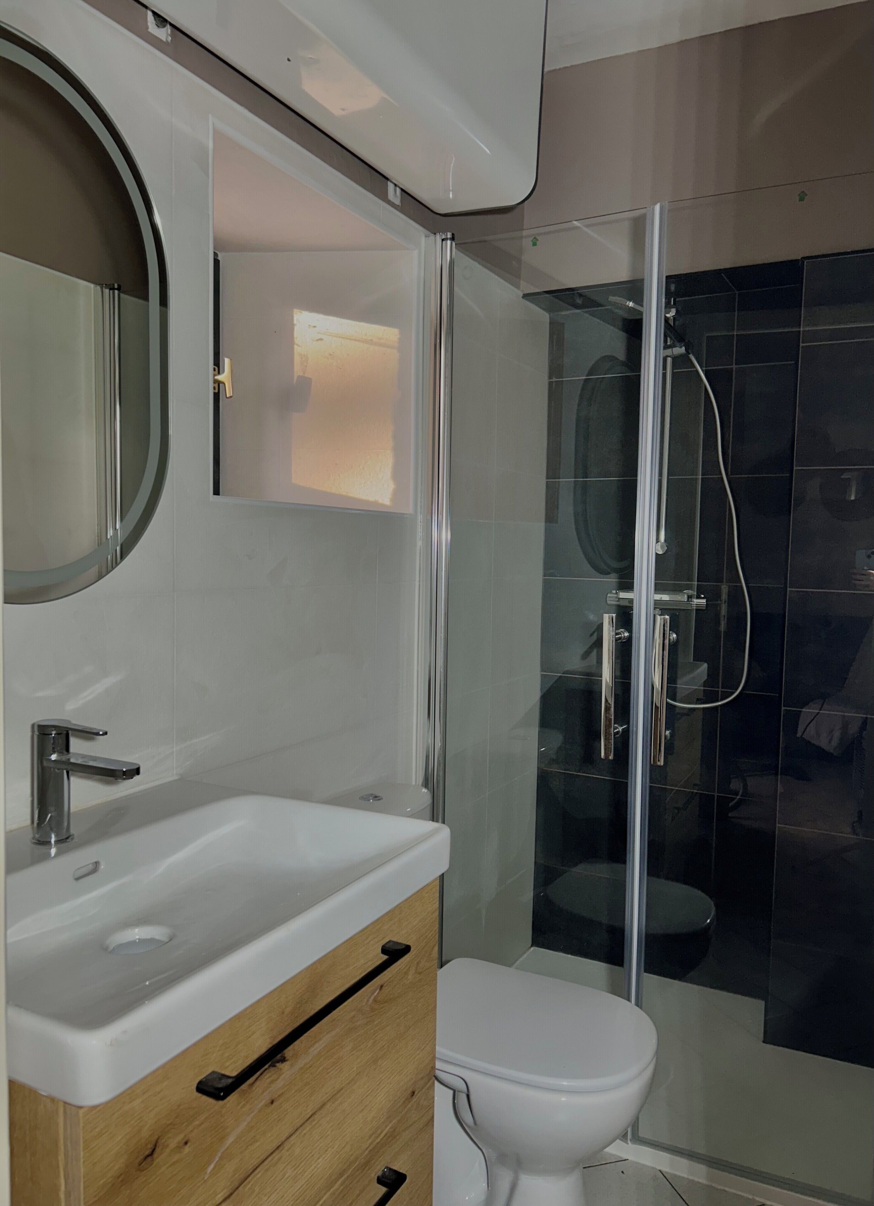 Une salle de bain moderne avec une douche à l’italienne en verre, un lavabo blanc et un meuble-vasque en bois.
