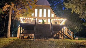 En træhytte med et stejlt tag, en veranda med gelænder og en trappe op til indgangen.