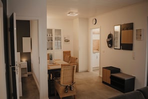 Eine moderne Küche mit weißen Schränken, einem Essbereich mit einem Korbstuhl und einem kleinen Holzschrank.