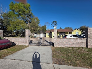 A gated driveway leading to a yellow house with a brick wall and a garage.