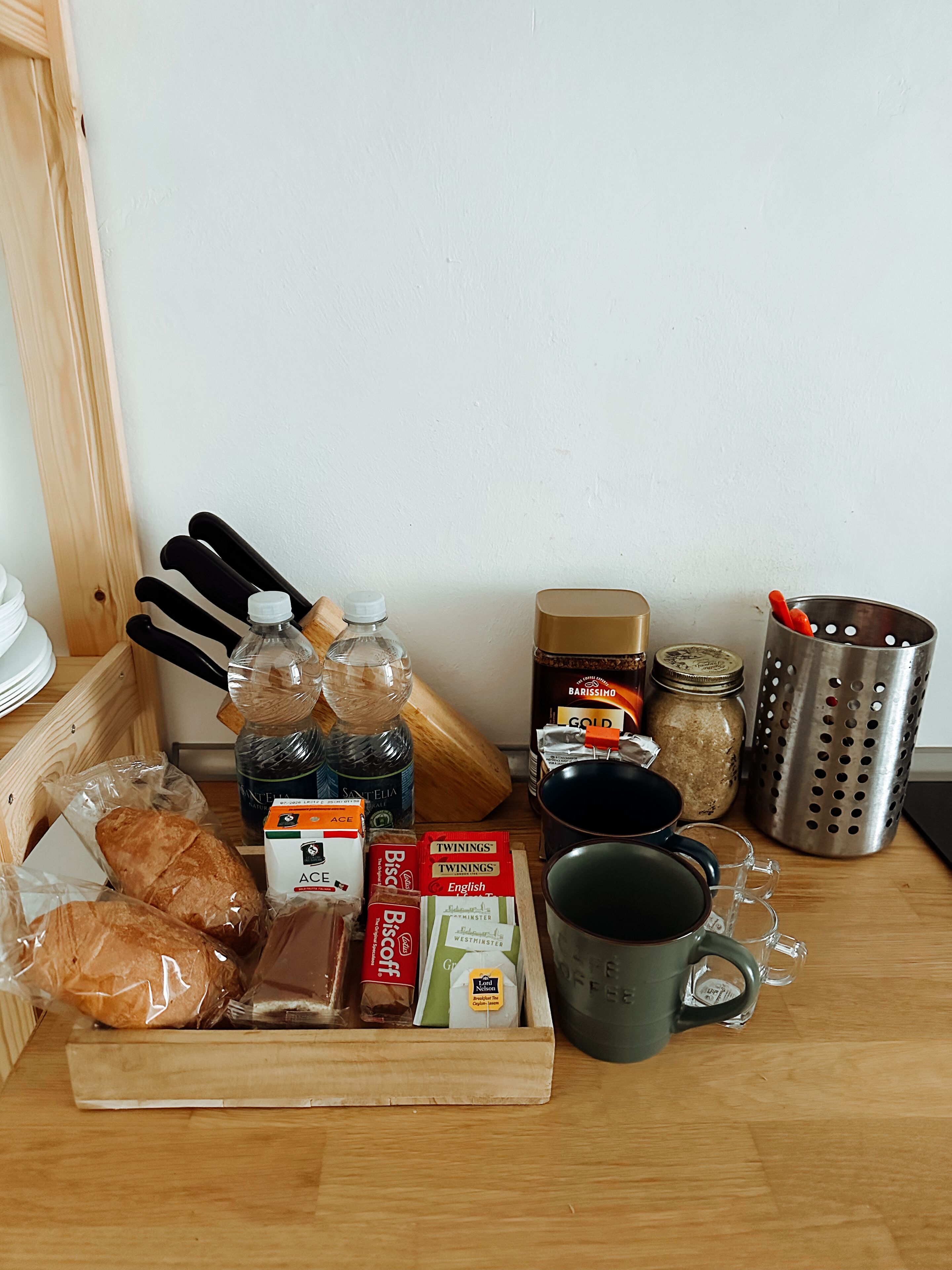 Ein Holztisch mit verschiedenen Speisen, darunter Brot, Gebäck und verpackte Waren, sowie Küchenutensilien und Behälter.