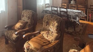 Un soggiorno con due poltrone imbottite, un mobile in legno, un tavolo da pranzo con sedie e un lampadario.