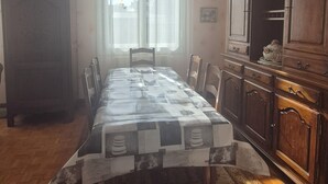 Una sala da pranzo con un lungo tavolo, sedie, un lampadario, una finestra con tende e un armadio in legno.