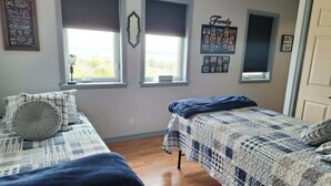 Ein Schlafzimmer mit zwei Betten, einem Fenster mit Jalousien, einer Wand mit dem Schriftzug 'Family' und einer Tür.