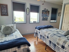 A bedroom with two beds, a window with blinds, a wall with a 'Family' sign, and a door.