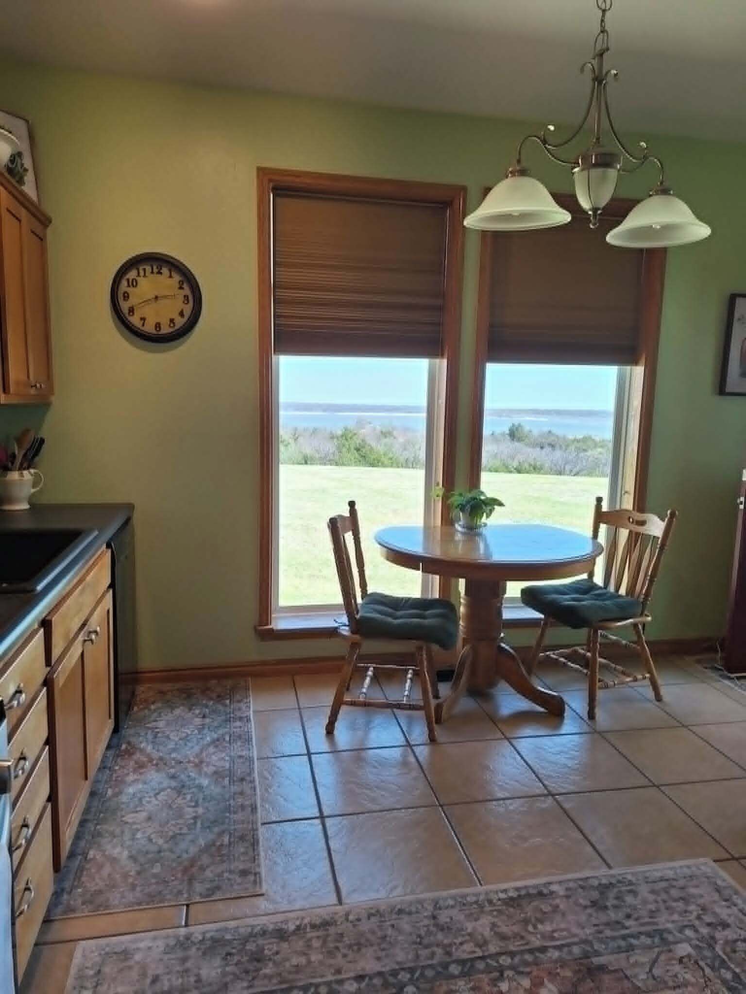 Une cuisine avec une table à manger, des chaises, une horloge et une vue sur l’extérieur.