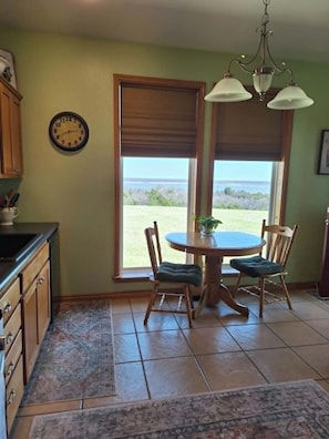A kitchen with a dining table, chairs, a clock, and a view of the outdoors.
