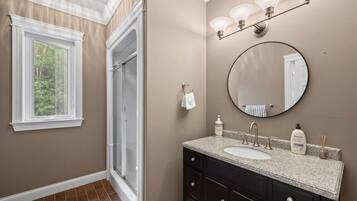 A bathroom with a large window, a shower, a sink with a vanity, and a mirror.